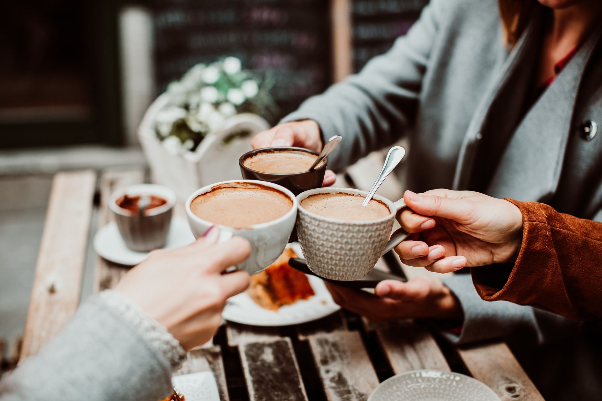 .Group of young friends drinking coffee with cakes in an outdoor cafe in Porto, Portugal. Holding their cups together. Close up. Lifestyle..